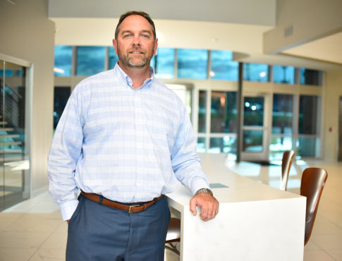 a man in a blue and white pin stripped shirt posing in front of a desk.